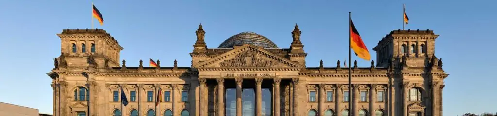 რაიხსტაგის შენობა ბერლინში გერმანიის დროშებით ცისფერი ცის ფონზე