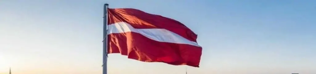 ლატვიის დროშა მზის ჩასვლისა და ცისფერი ცის ფონზე