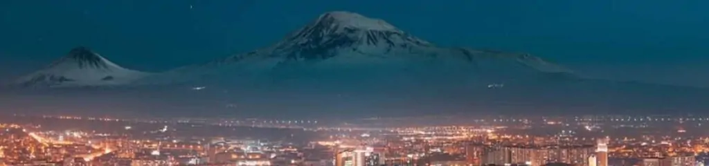 ღამის პანორამა, სადაც ცენტრში ჩანს ზღვის დონიდან მაღალი მთა თოვლით დაფარული, ხოლო ქვემოთ განათებული ქალაქის ხედი